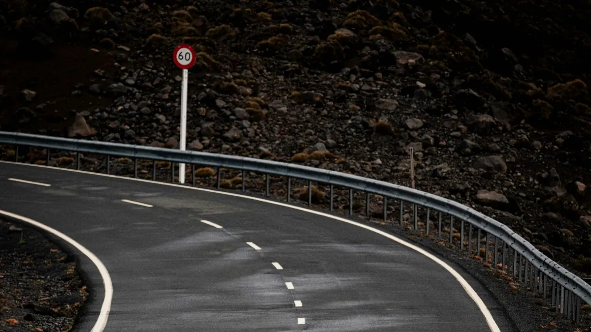 A winding mountain road bordered by a metal guardrail and speed limit sign