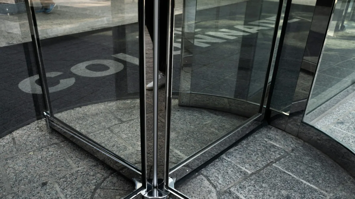 Close-up of a glass revolving door showing its central spindle, angled panels, and circular floor track